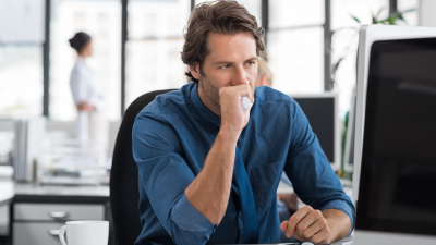 a stressed out man sits at a desk and looks at a monitor, holding a handkerchief tightly in his fist