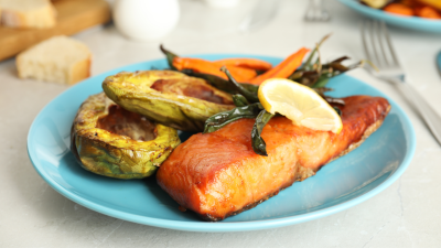 a nutritious meal inluding grilled salmon, vegetables, and avocado on a blue plate