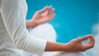 close up view of a woman in a seated yoga pose, only her hands, forearm, and knees are in the frame